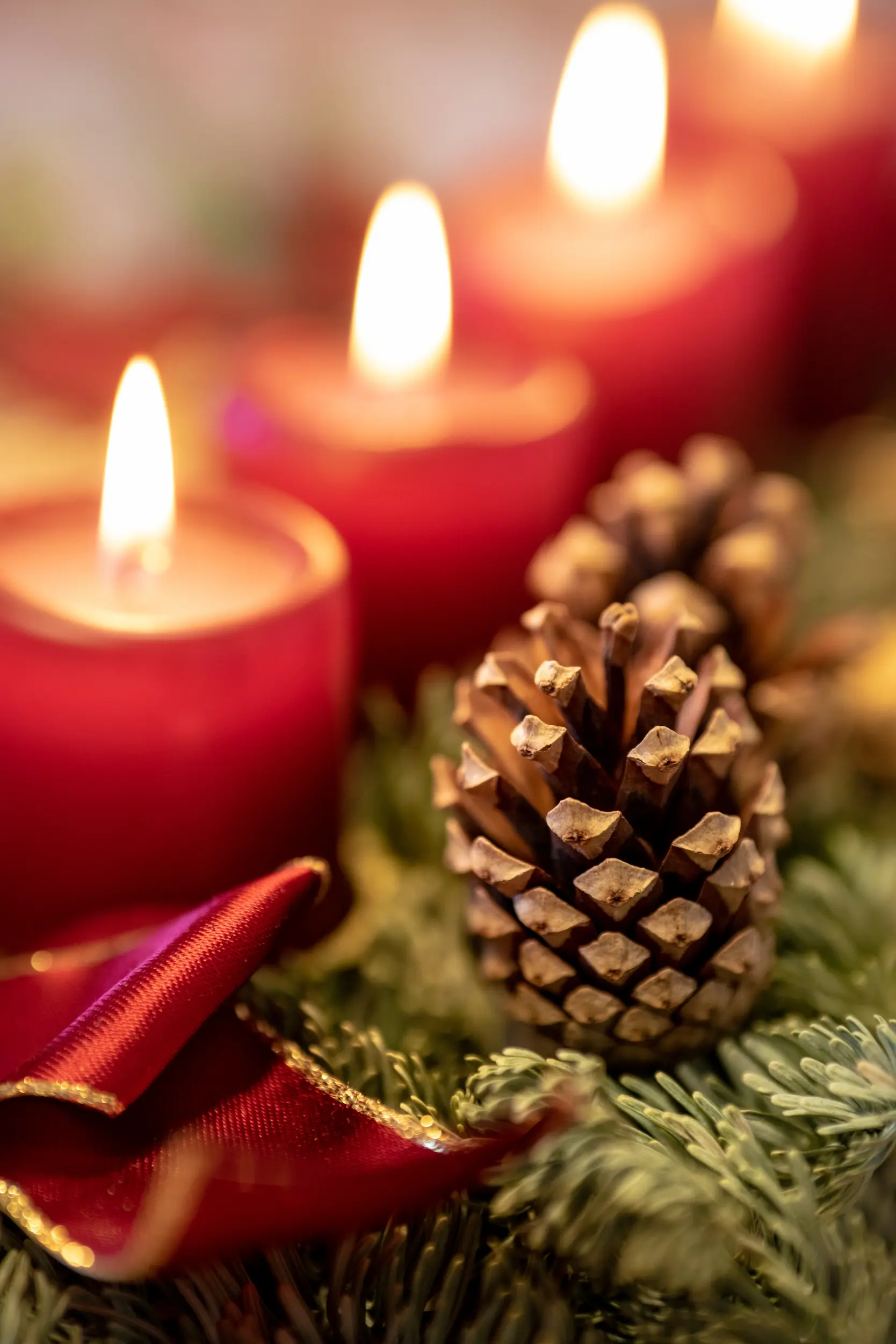 Rote Kerzen eines Adventkranzes die brennen und von Zapfen und Bändern umgeben sind.